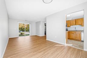 A room with wooden floors and white walls, leading to a kitchen area.