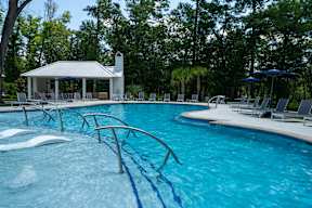 A pool with a diving board and a pavilion in the background.