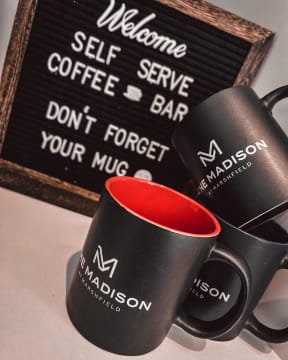 two black coffee mugs in front of a black sign that says welcome self serve coffee bar
