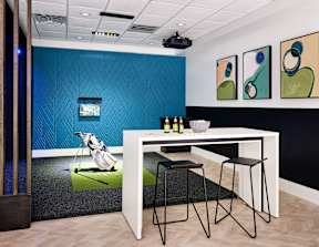 a room with a table and chairs in front of a golf simulator