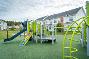 a playground with slides and monkey bars in front of a row of houses