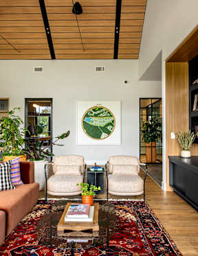 A living room with a rug, two chairs, a couch, and a painting on the wall.