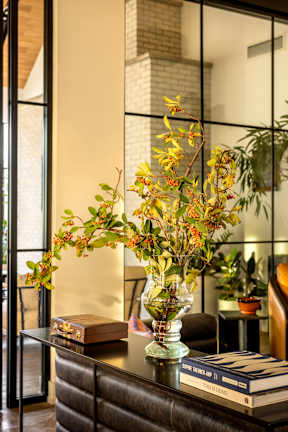 A vase with flowers sits on a table in front of a glass wall.