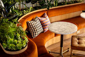 A round table with a white marble top is in the middle of an orange couch.