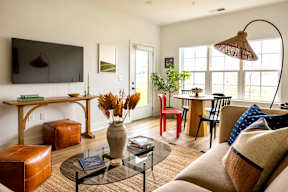 A living room with a brown sofa, a glass coffee table, and a red chair.