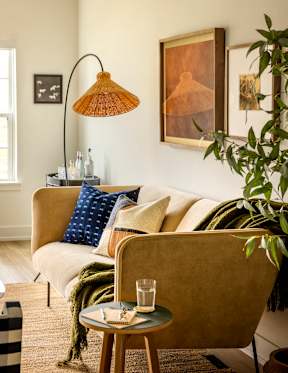 A living room with a beige couch, a small table with a glass of water, and a lamp.