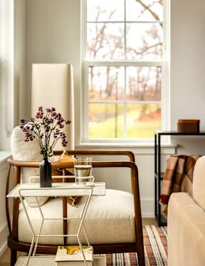 A table with a vase of flowers and a glass of water sits in front of a window.