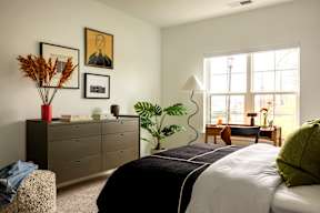 A bedroom with a large bed, a dresser, a chair, and a window.