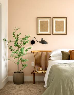 A bedroom with a bed, a bench, a potted plant, and two pictures on the wall.