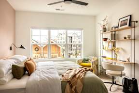 A bedroom with a large bed and a window overlooking a residential area.