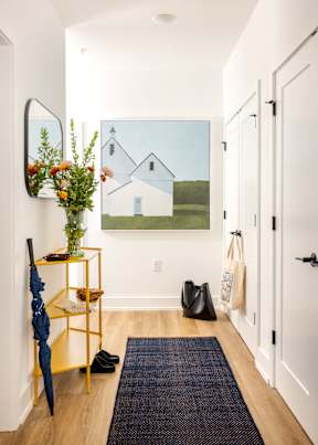 A hallway with a yellow rack and a painting of a house on the wall.
