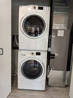 A white front load washing machine with a black control panel is stacked on top of a silver dryer.