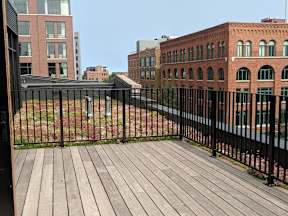 A wooden deck with a black railing in the foreground with a view of a cityscape in the background.