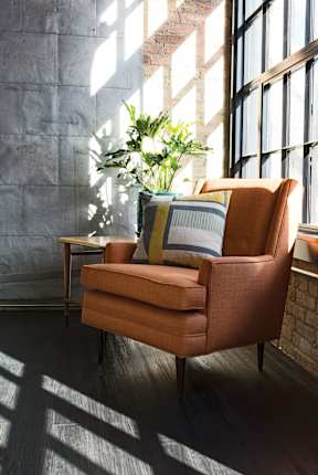 A brown chair with a striped pillow is in front of a window.