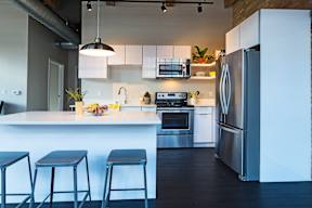 A modern kitchen with a white counter and bar stools.