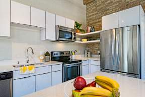 A kitchen with a white counter top and a bowl of fruit on it.