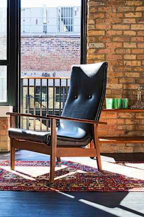 A black leather chair with wooden legs sits in front of a window.