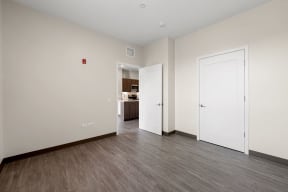 a bedroom with white walls and wood flooring and a door to a kitchen