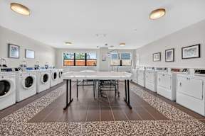 A laundry room with a table and chairs in the middle of washing machines.