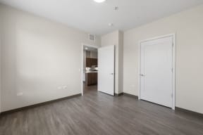 a bedroom with white walls and wood flooring and a door to a bathroom