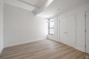 A room with white walls and wooden flooring, with a window on the right side.