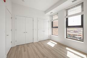 A room with white walls, wooden floors, and a large window with blinds.