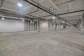 A large parking garage with a concrete floor and exposed ceiling pipes.