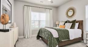 A bedroom with a bed, a dresser, and a window with curtains.