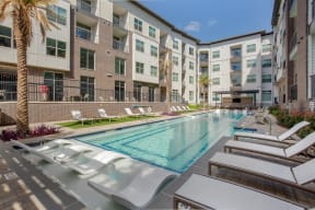a swimming pool with lounge chairs in front of an apartment building