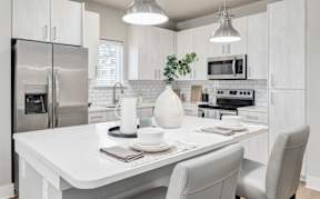 A modern kitchen with a white table and grey chairs.