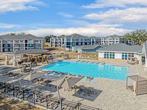 A large swimming pool surrounded by sun loungers and umbrellas with a building in the background.