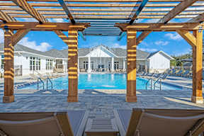 A wooden pergola over a swimming pool with lounge chairs underneath.