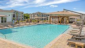 A large swimming pool with a sun lounger area and a building in the background.