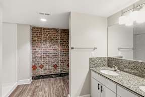 A bathroom with a brick wall and wooden floors.