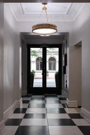 A hallway with black and white checkered flooring and a chandelier hanging from the ceiling.