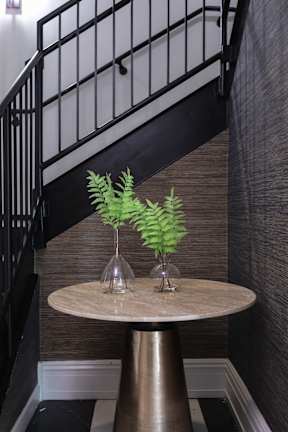 A plant in a vase sits on a table in front of a staircase.