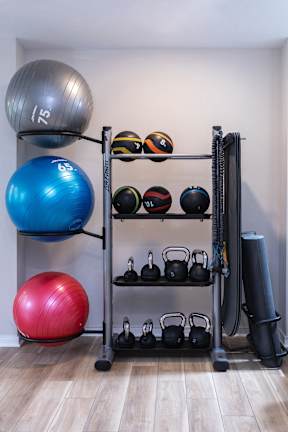 A gym with a blue ball, a red ball, a silver ball, and a rack with kettlebells and other balls.