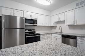 A kitchen with a refrigerator, oven, microwave, and sink.