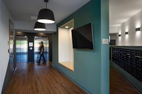 A hallway with a person walking in the distance and a TV mounted on the wall.
