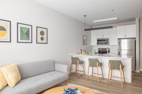 A modern living room with a grey couch and a kitchen area in the background.