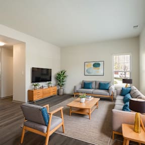 A living room with a grey couch, a wooden chair, a wooden coffee table, a wooden cabinet, a flat screen TV, a potted plant, and a painting on the wall.