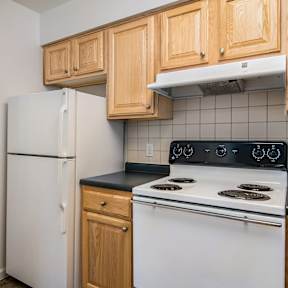 A kitchen with a white refrigerator, white stove, and wooden cabinets.