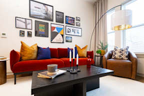 A living room with a red couch, a black coffee table, and a collection of framed pictures on the wall.