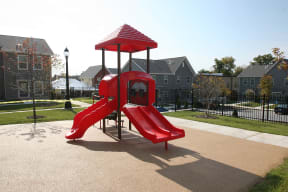 a playground with a red slide and umbrella in a park