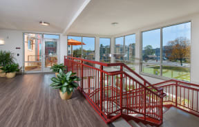 a stairway with red railings and a potted plant in front of windows at Cornerstone Village Apartments