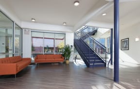 a Community room with orange couches and a blue staircase at Cornerstone Village Apartments