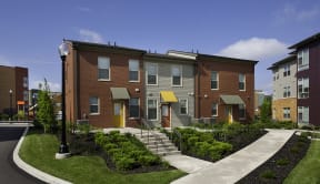 a row of brick apartment buildings with stairs and landscaping at Cornerstone Village Apartments