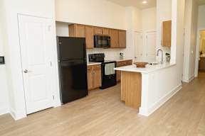 A black refrigerator is in the corner of a kitchen.