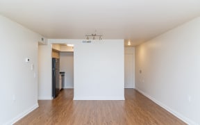 an empty living room with a white wall and wood floors at Crawford Square Apartments & Townhomes