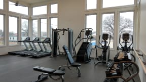 a fitness room with cardio equipment and large windows